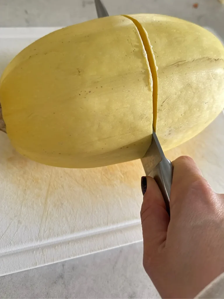 Cutting the spaghetti squash crosswise with a knife on a cutting board.