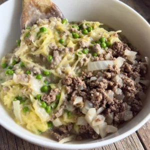 Creamy garlic spaghetti squash with ground beef and peas in a large bowl with a wooden spoon in it.