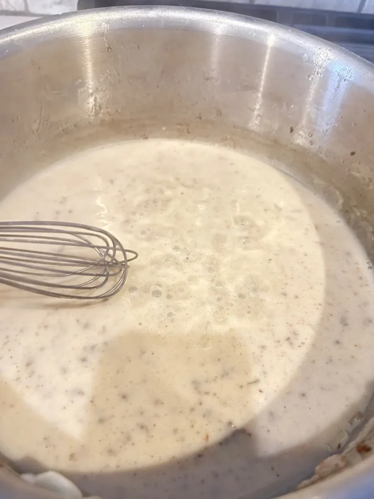 Whisking the milk into the pot of butter and flour on the stove.