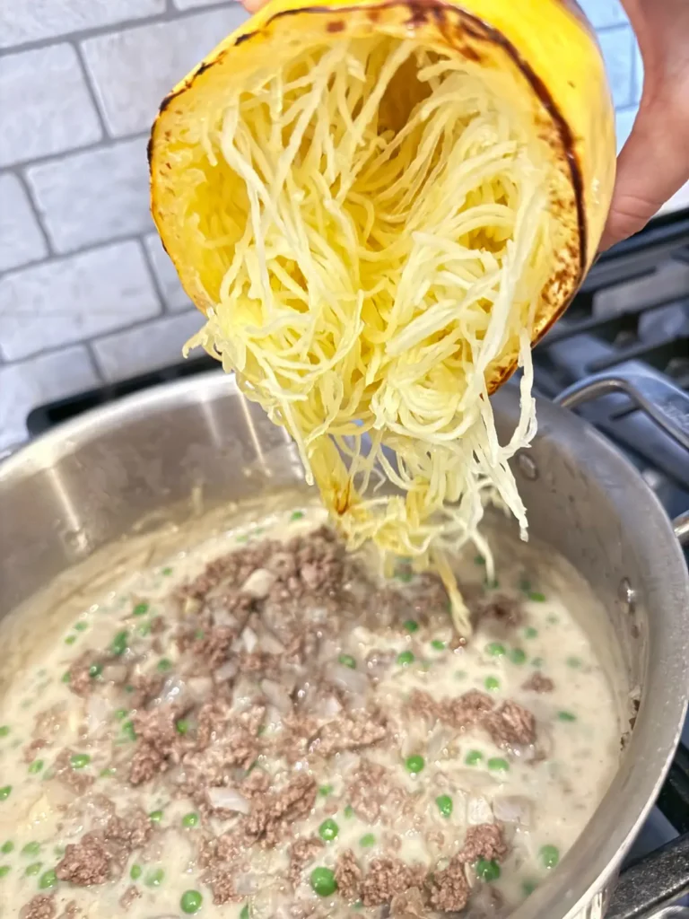 Pouring the spaghetti squash strands into the cream sauce on the stove.