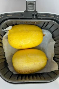 Two spaghetti squash halves turned over in an air fryer basket.