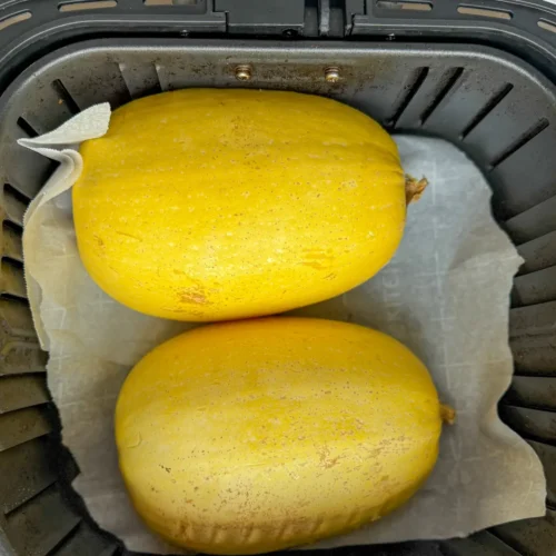 Two spaghetti squash halves turned over in an air fryer basket.