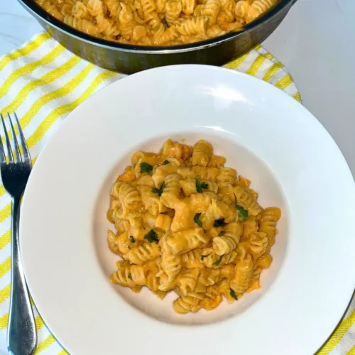 A bowl of cottage cheese mac and cheese on a yellow towel next to a fork.
