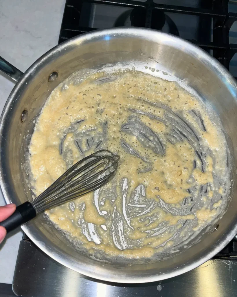 Making a roux of flour and butter in a pan with a whisk.
