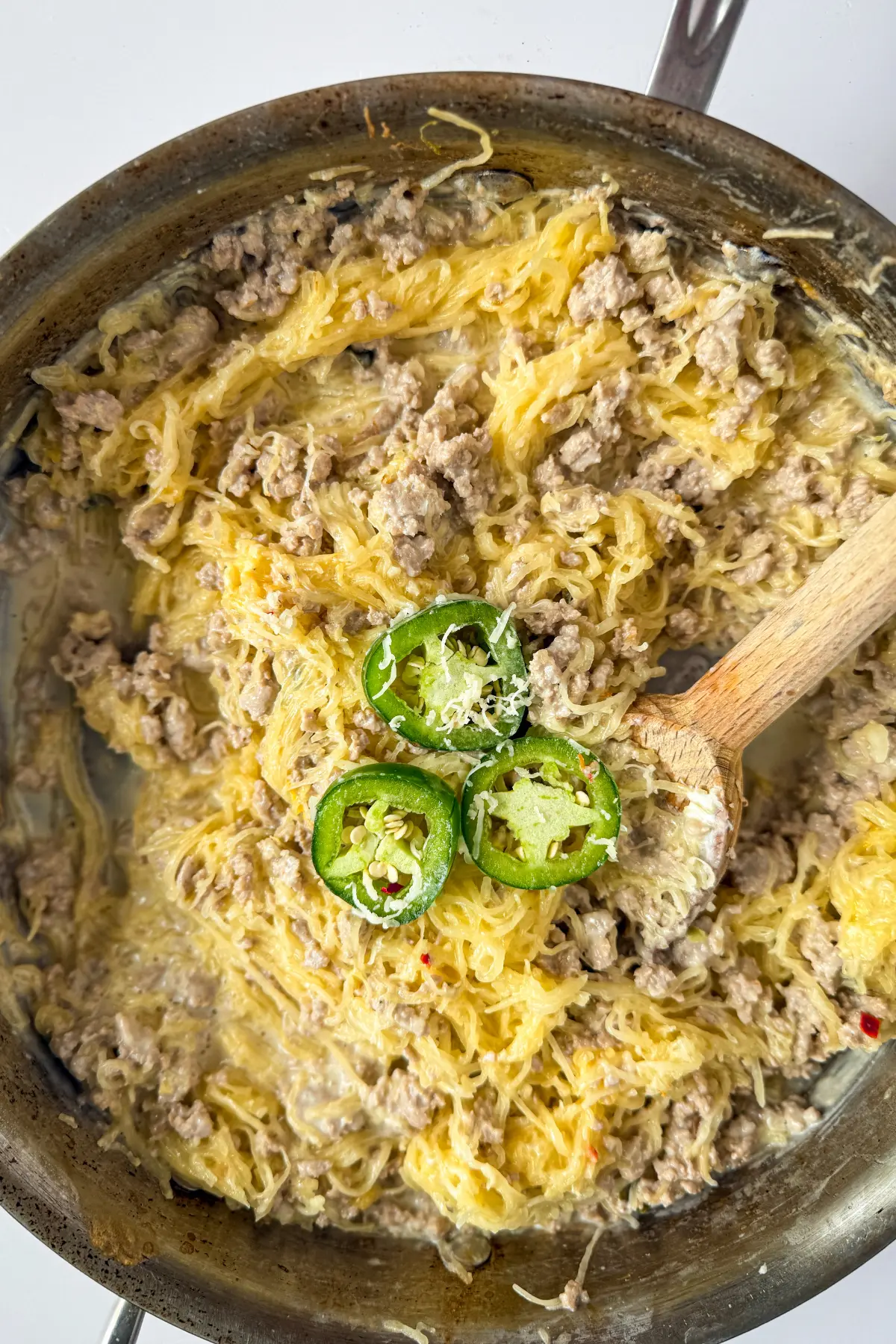 A birds-eye view of a pan of creamy garlic spaghetti squash with a wooden spoon in it and three jalapeno slices on top.