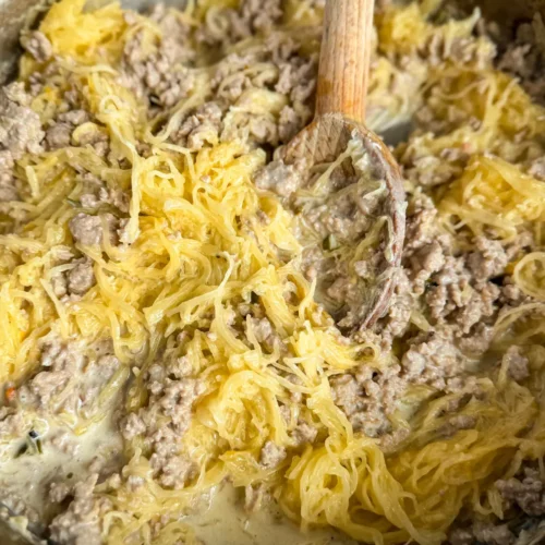 A birds-eye view of a pan of creamy ground turkey spaghetti squash with a wooden spoon stirring it.