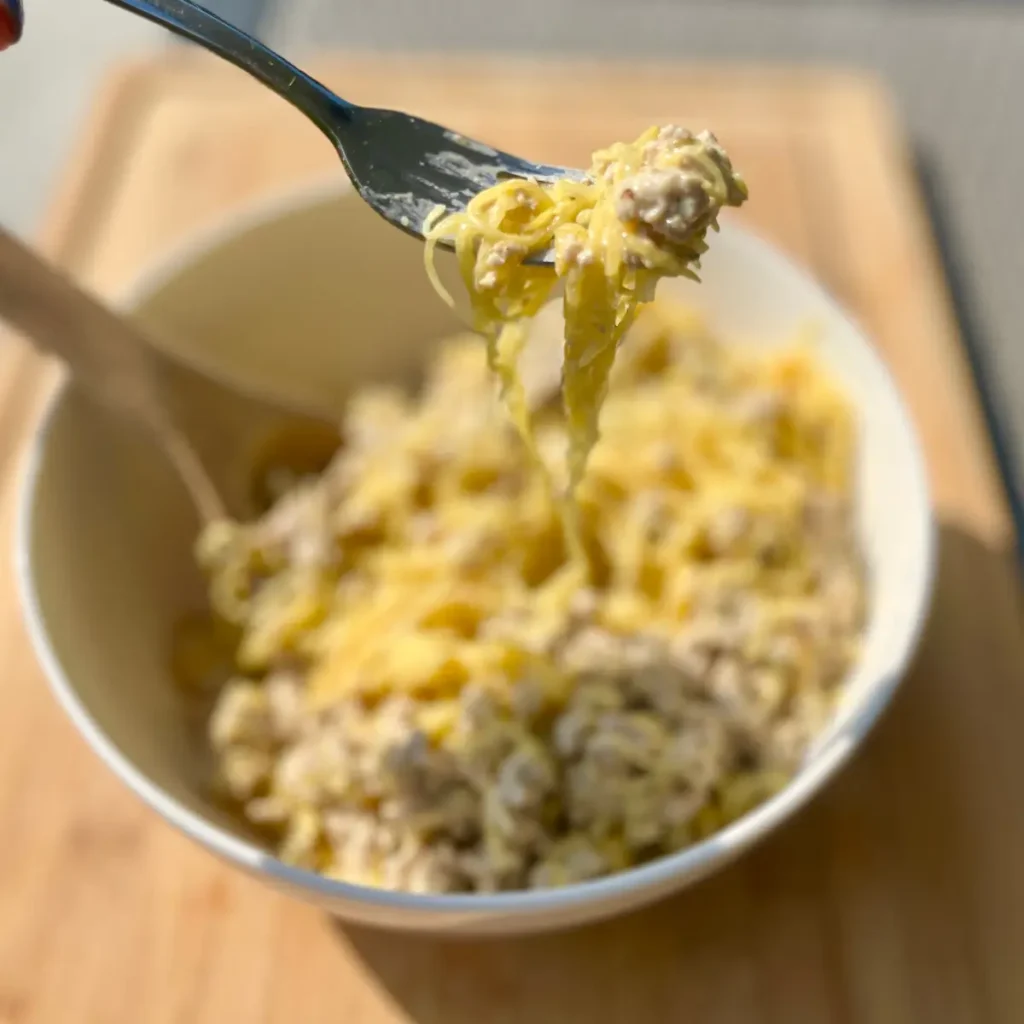 A close-up of a spoonful of the creamy ground turkey spaghetti squash with a large bowl of it in the background.