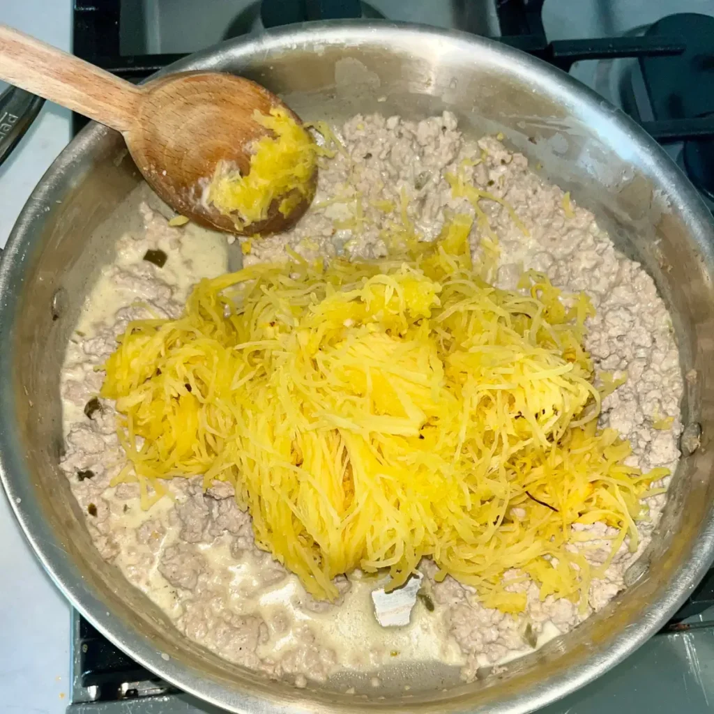 A pan with ground turkey and the creamy sauce with the spaghetti squash strands on top, prior to mixing.