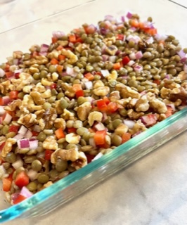 Lentil salad with chopped walnuts and bell peppers in a glass storage container.