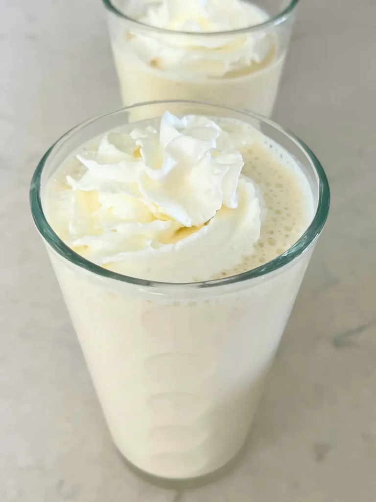 Three glasses of banana protein smoothies topped with whipped cream on a counter.