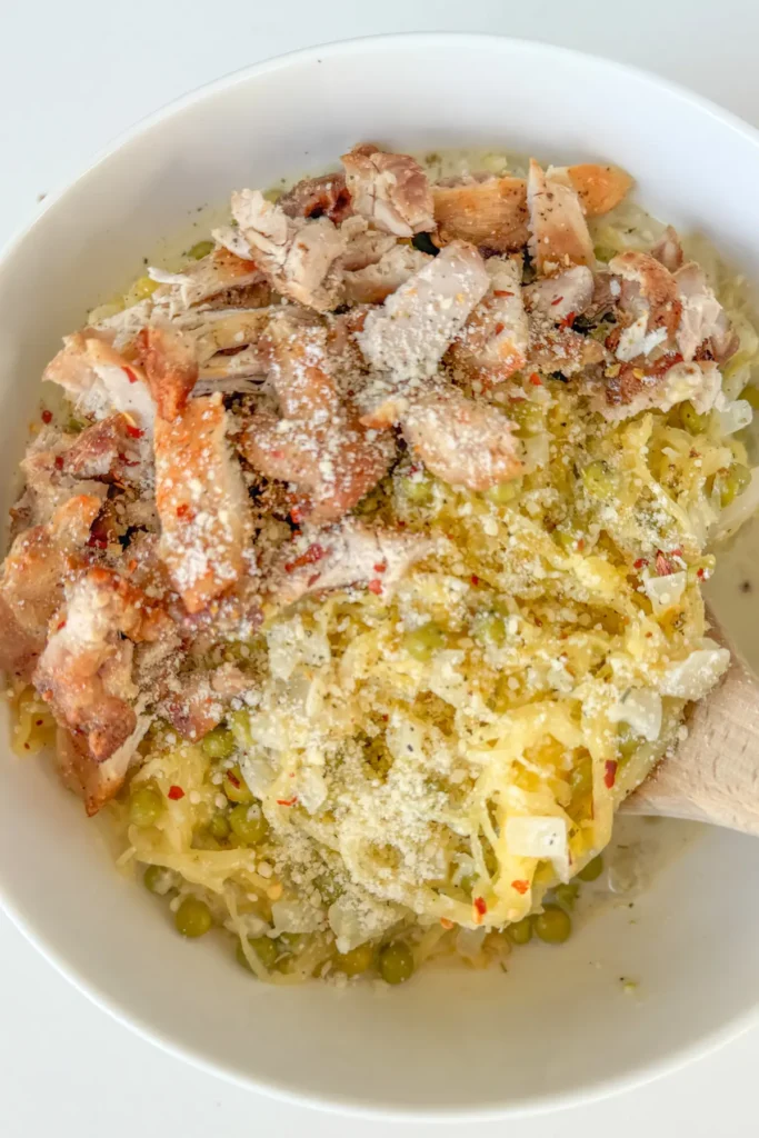 A birds-eye view of cottage cheese Alfredo spaghetti squash with diced chicken thighs in a large white bowl.