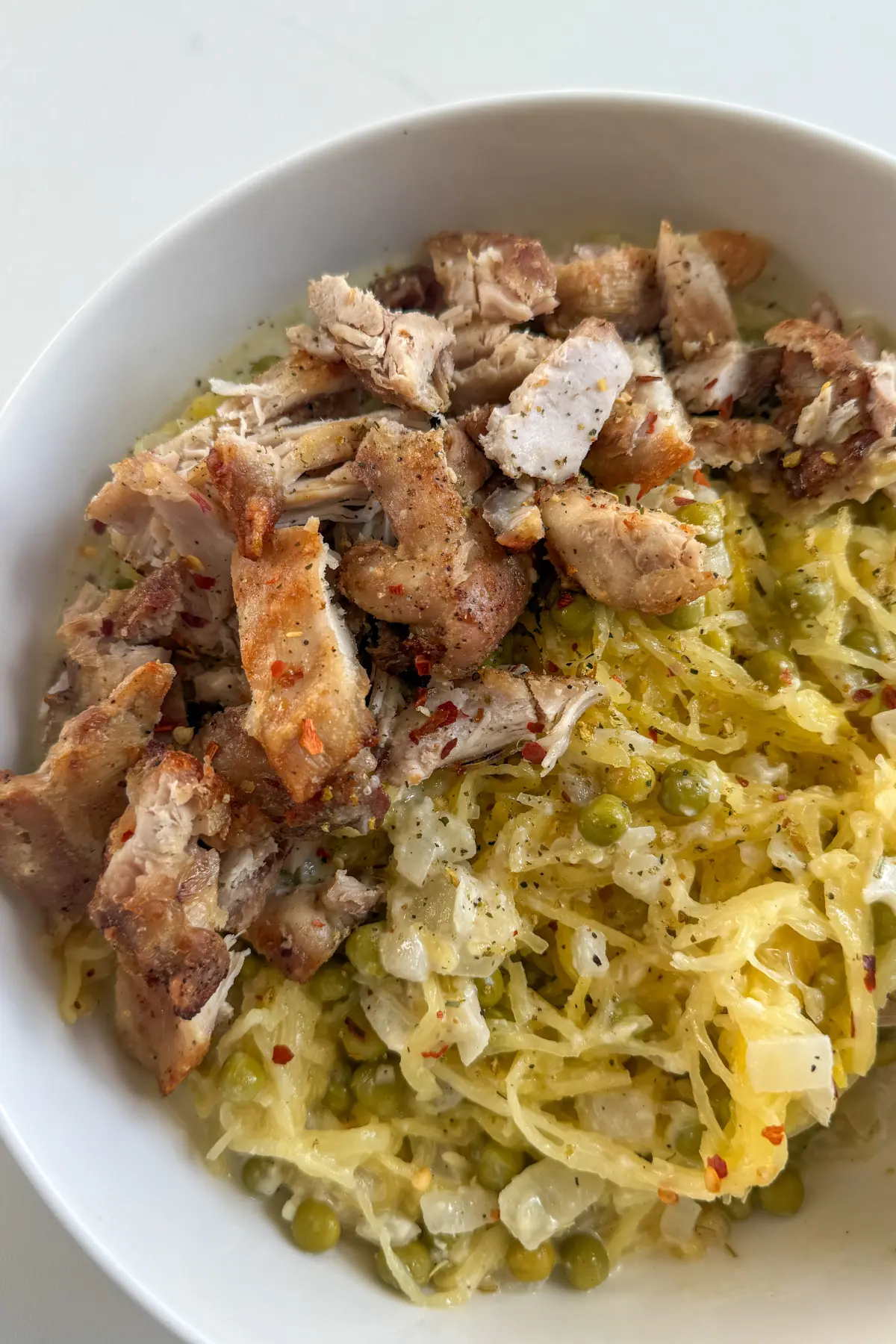 A fully assembled bowl of diced chicken thighs, spaghetti squash, and a cottage cheese Alfredo sauce.