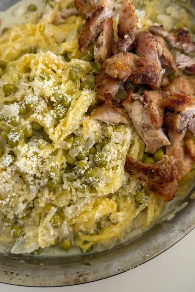 A close-up of the cottage cheese Alfredo spaghetti squash topped with parmesan next to diced chicken thighs in a stainless steel pan. 