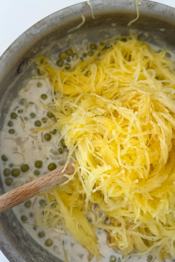 Adding spaghetti squash strands to the Alfredo sauce in a pan.