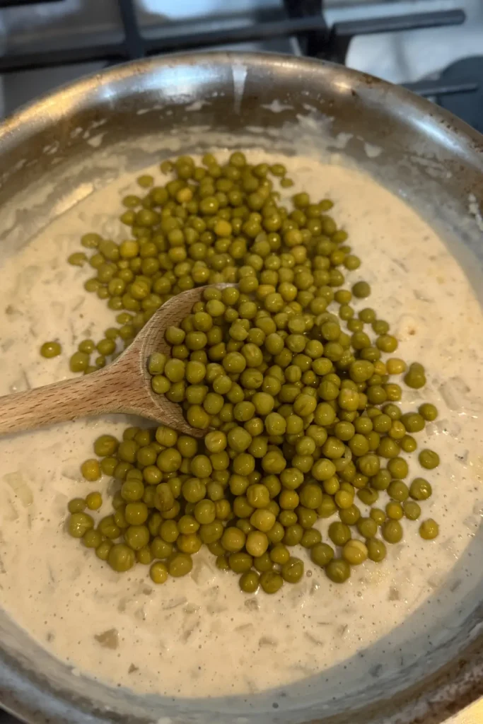 Adding the peas to the cottage cheese sauce in a pan.