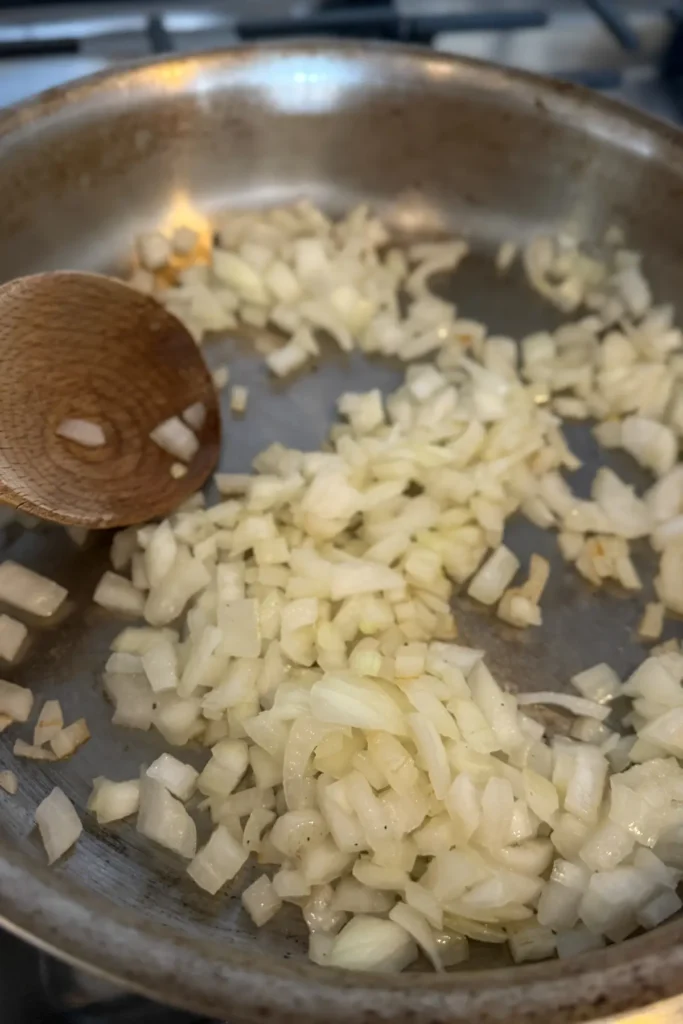 Sauteeing diced onions in a stainless steel pan with a wooden spoon. 