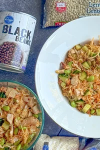 A can of black beans, a bag of lentils, and two bowls of Asian rice salad on a counter.
