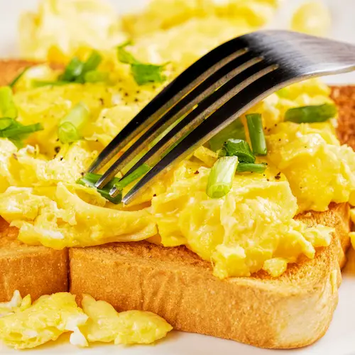 Scrambled eggs on toast with a fork digging into it.
