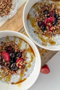 Two chia breakfast bowls topped with fruit and chopped nuts.