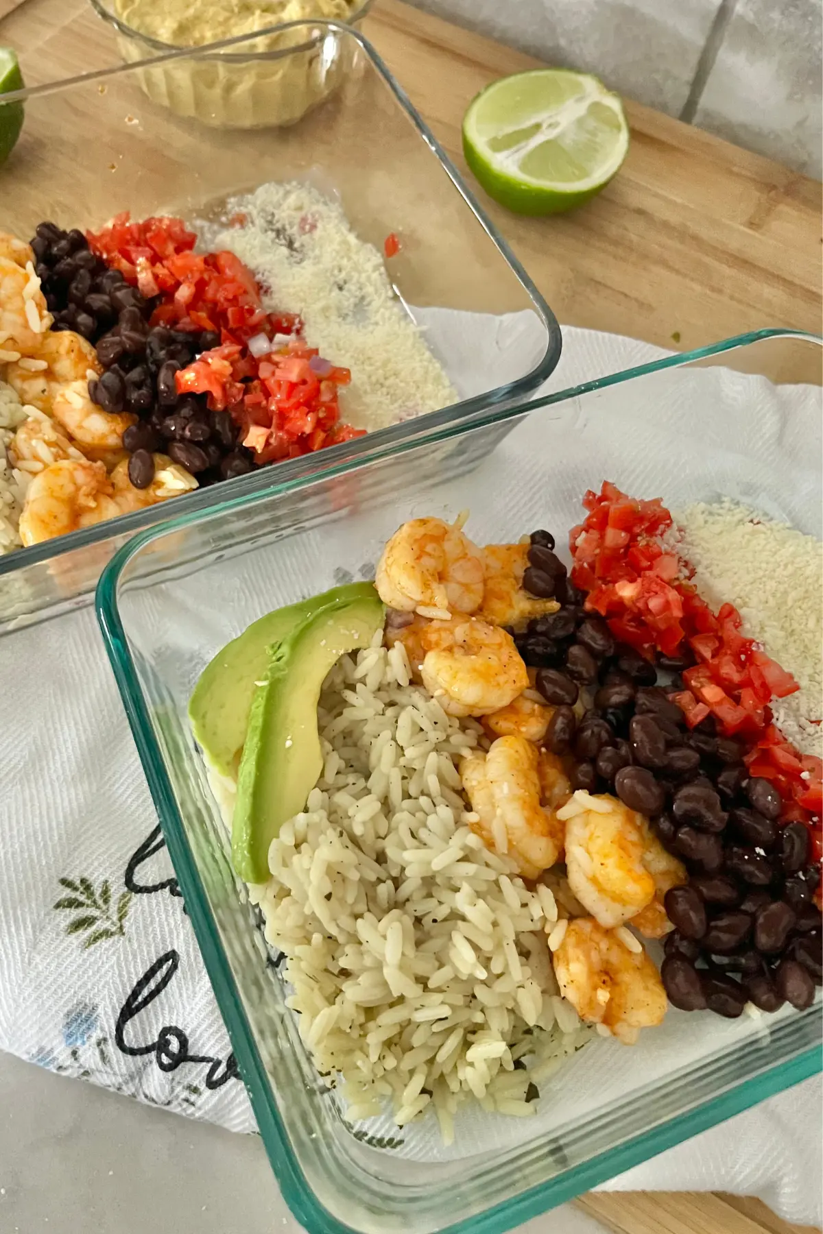 Two shrimp taco bowls assembled in meal prep containers on a wooden cutting board.