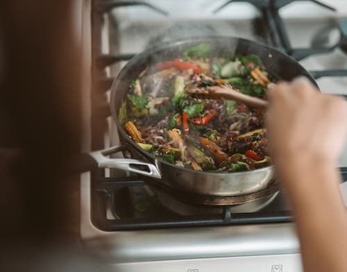 A stir-fry on the stove being mixed with a wooden spoon.