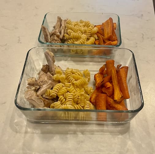 Two storage containers of diced sweet potatoes, chicken and pasta.