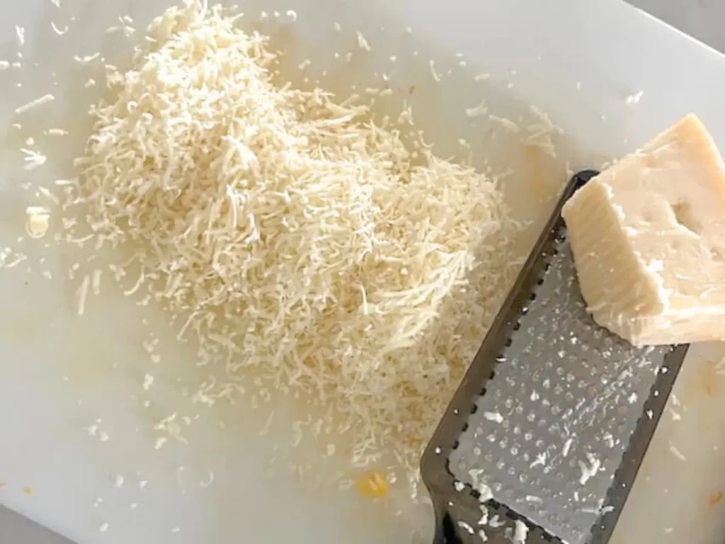 A cutting board with grated parmesan cheese on it.