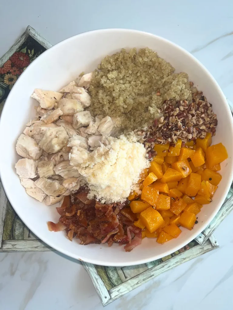 A large bowl of butternut squash, quinoa, bacon, parmesan, pecans and chicken on a counter.