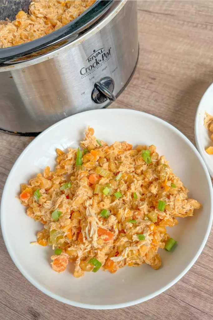 A plate of buffalo chicken cottage cheese pasta next to a slow cooker on a table.