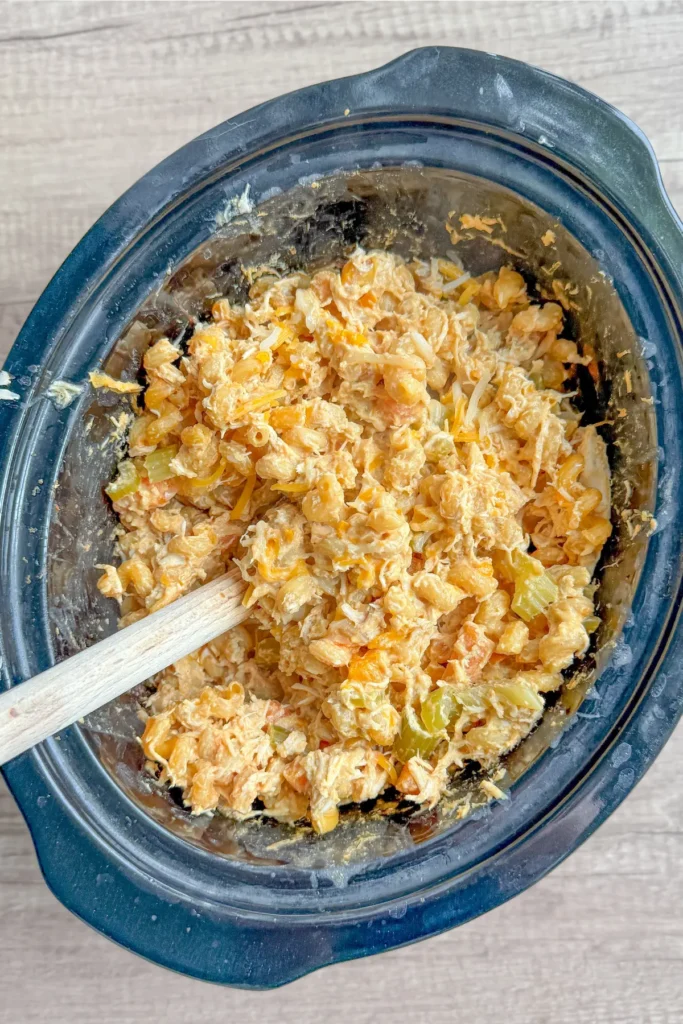 A birds-eye view of the buffalo chicken pasta in a slow cooker after cooking with a wooden spoon in it on a table.