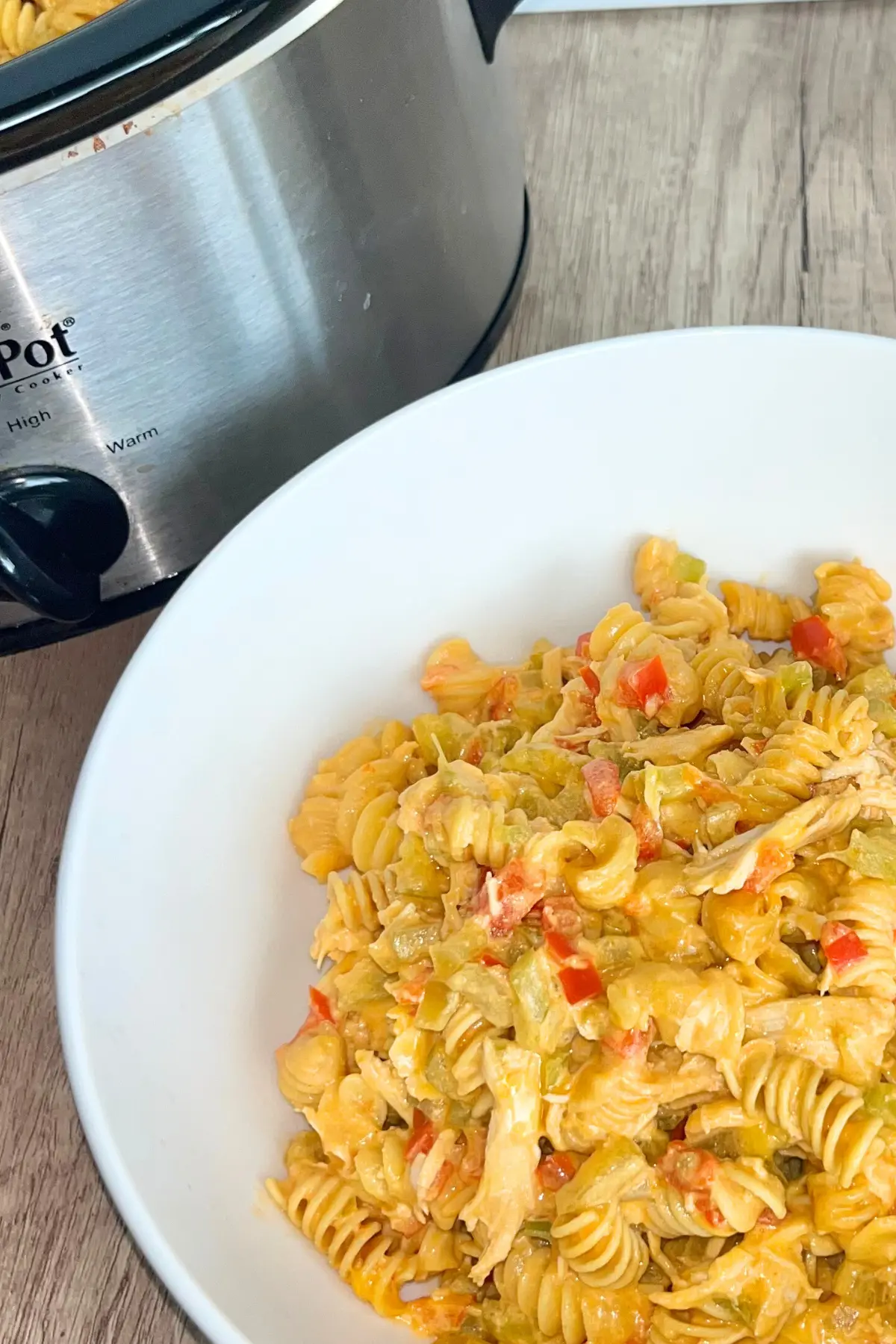 A big bowl of high protein buffalo chicken pasta next to a crockpot on a counter.