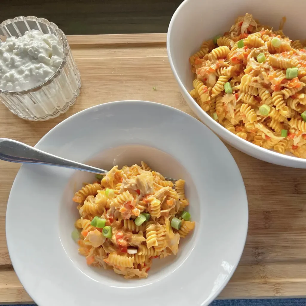 A small bowl of buffalo chicken crockpot pasta next to a larger bowl on a cutting board.