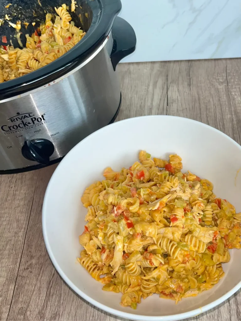 A large bowl of buffalo chicken crockpot pasta with cottage cheese on a counter next to a crockpot.