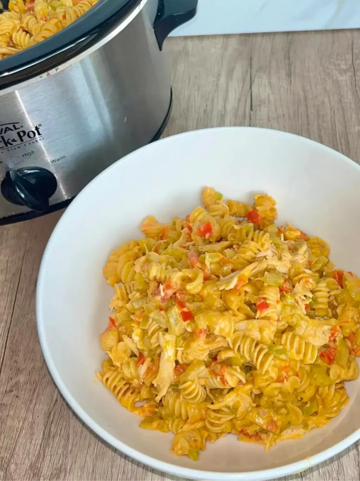 A large bowl of creamy buffalo chicken pasta with cottage cheese on a counter next to a slow cooker.