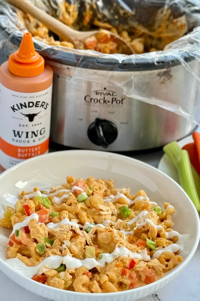 A bowl of buffalo chicken pasta next to a large crockpot on a counter.
