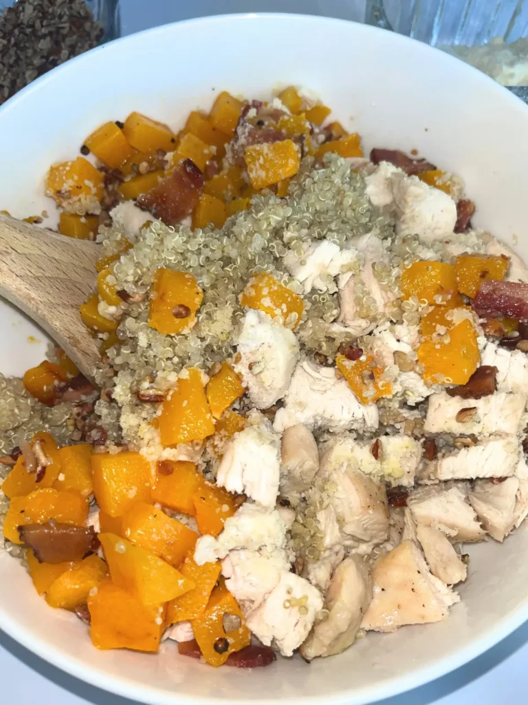 A close-up of a mixed up butternut squash quinoa bowl with a wooden spoon in it.