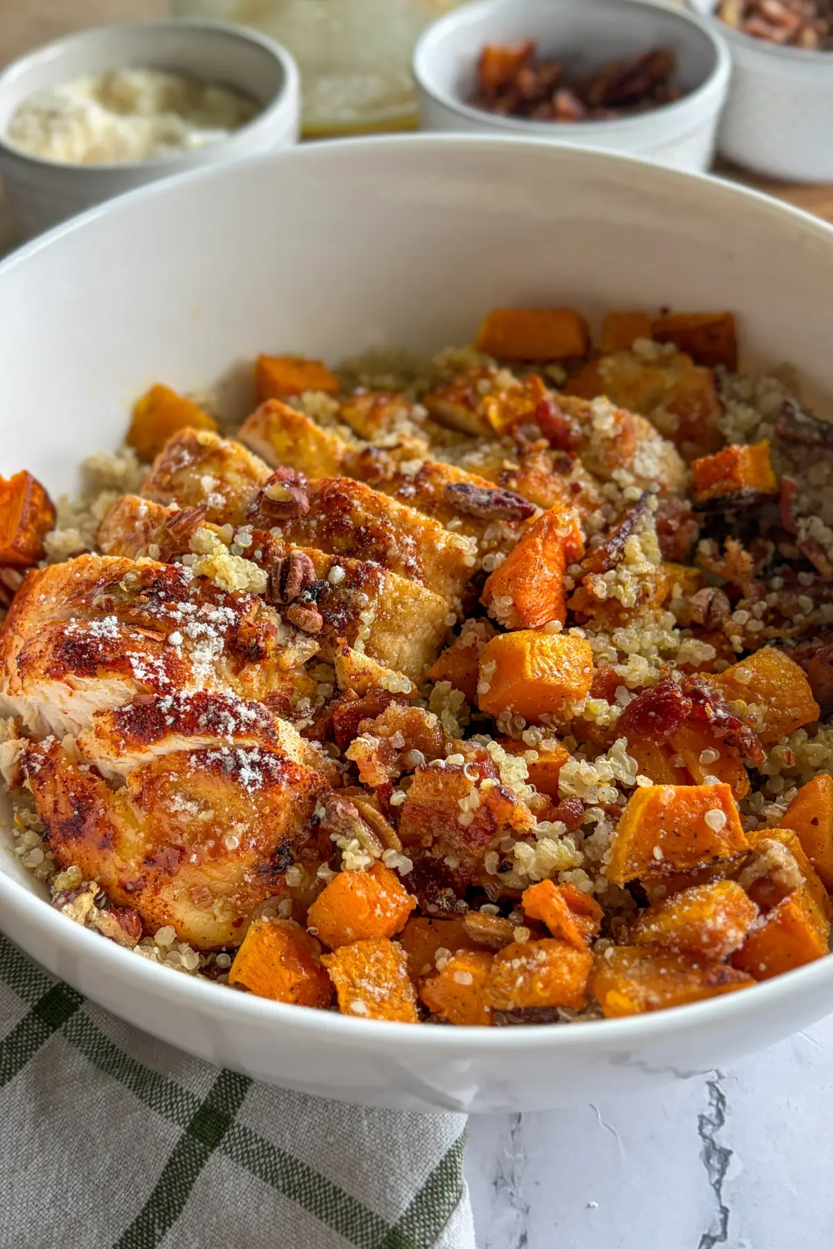 A fully assembled butternut squash quinoa bowl in a large white bowl on a table next to a bowl of pecans.