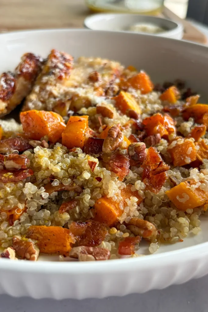 A close-up of a plate filled with quinoa, roasted butternut squash, pecans, parmesan cheese and chicken with a fork on it.