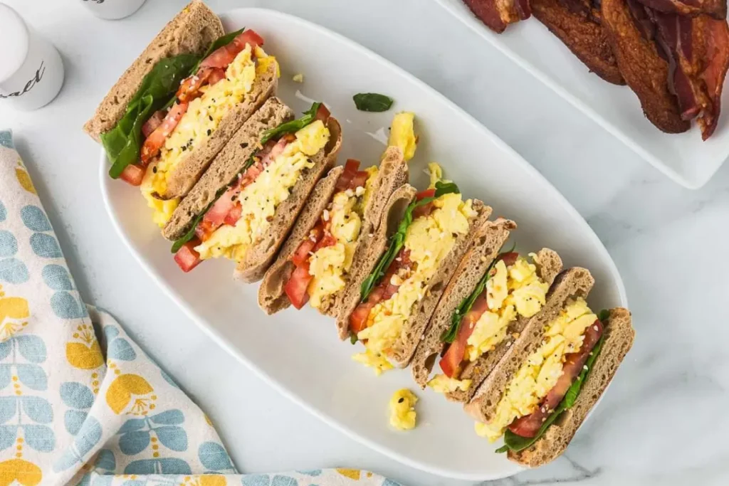 Cottage cheese and scrambled egg sandwiches lined up on a white platter on a table.