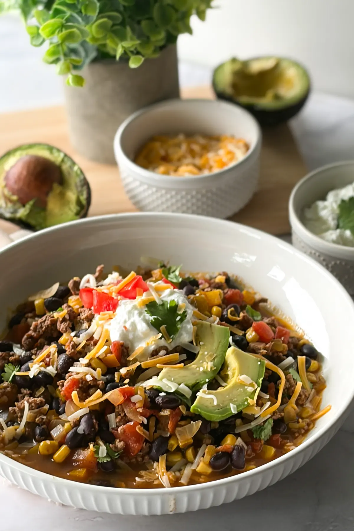 A bowl of Mexican chili topped with toppings on a table next to a bowl of shredded cheese.