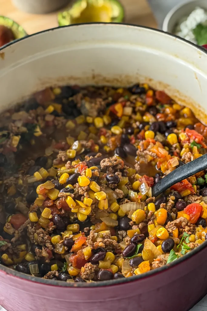 A big pot of cooked chili with a black ladle in it.