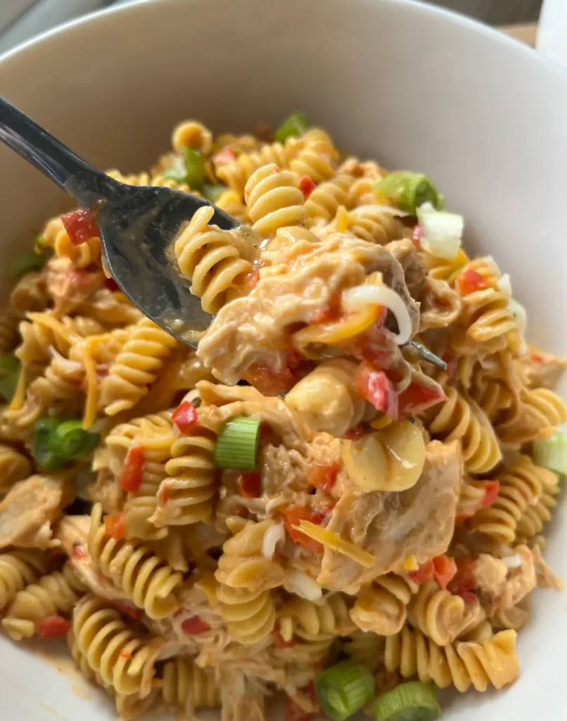 A bite on a fork of this healthier buffalo chicken pasta from a large bowl.