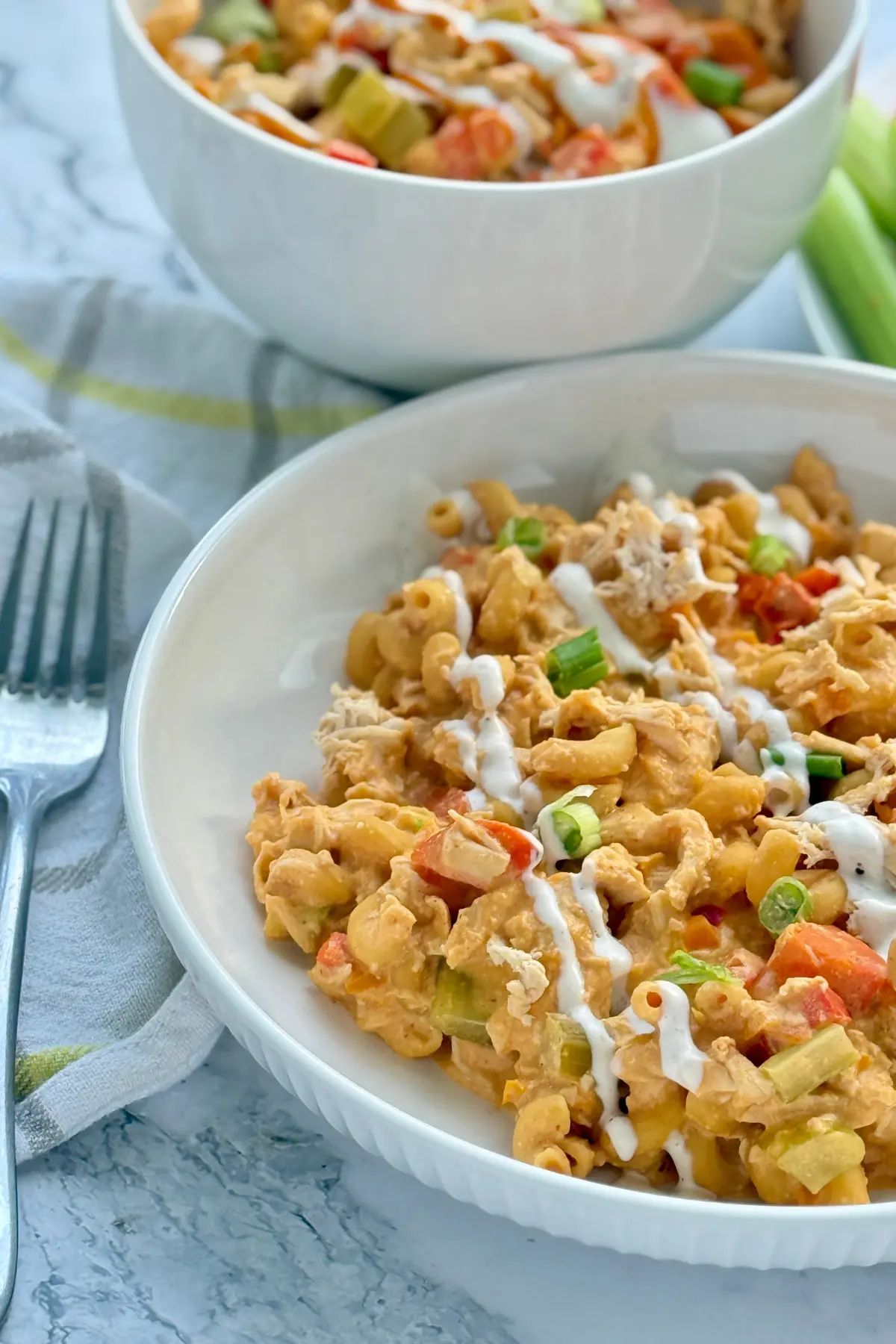 A bowl of buffalo chicken cottage cheese pasta drizzled with ranch on a table next to a fork.