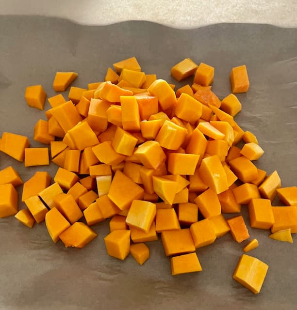 Diced butternut squash on a sheet pan lined with parchment paper.