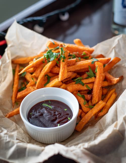 Sweet potato fries and BBQ sauce on parchment paper for high calorie food for kids.
