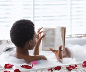 A mom prioritizing self-care by reading a book in the bath