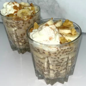 Banana cinnamon overnight oats with protein powder in two glass cups topped with whipped cream, banana slices and chopped nuts.