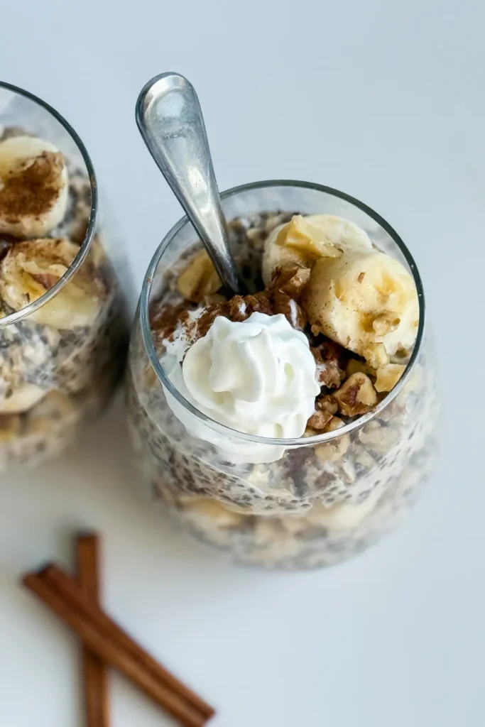 A birds-eye view of two glasses of banana cinnamon overnight oats wiht spoons in them on a counter.