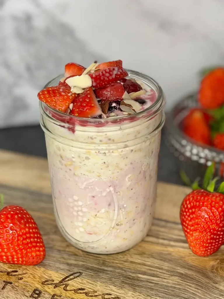 Overnight oats topped with strawberries and blueberries on a wood cutting board on the counter next to a bowl of strawberries.