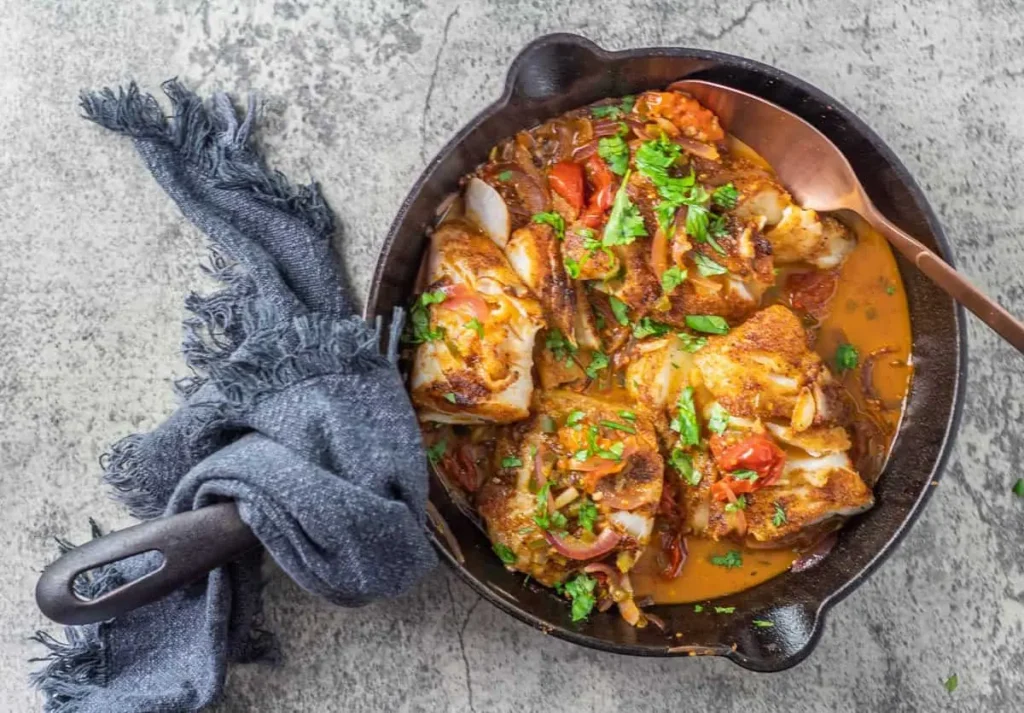 Pan seared Mexican fish in a cast iron skillet on a table next to a dish towel.